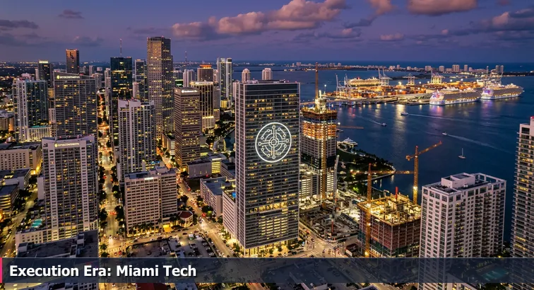 Twilight aerial of downtown Miami and Brickell with lit office towers, a high-rise bearing a Palantir logo, active construction cranes, and the port in the distance.