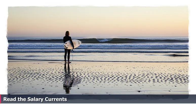 A surfer at dawn on Torrey Pines beach, studying ocean currents to symbolize strategic analysis of AI salaries in San Diego.